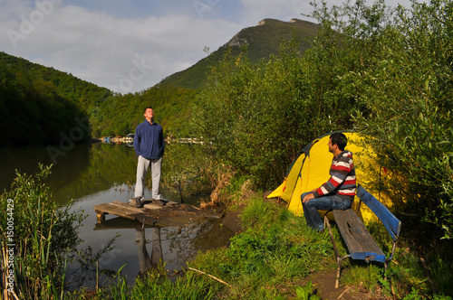 Young man camping by the river and get rest in nature. Morning on the river under a mountain