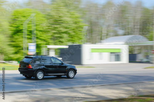 Black car in motion on asphalt road and green trees