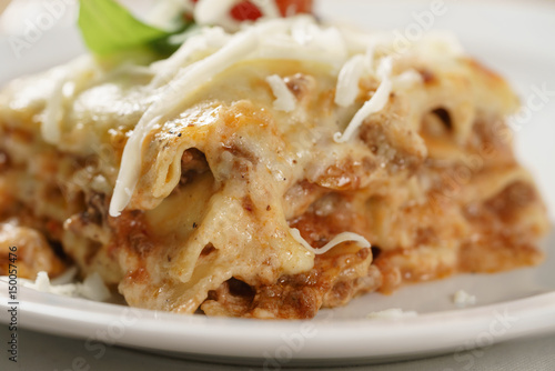 homemade lasagna portion on white plate on wood table, shallow focus