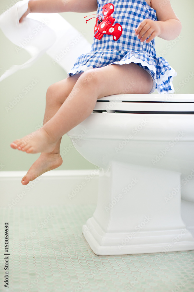 Neck down view of female toddler sitting on toilet seat pulling toilet
