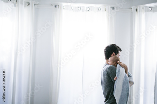 Mid adult man carrying baby son in living room