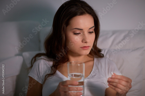 Billede på lærred woman with pill and glass of water in bed at home