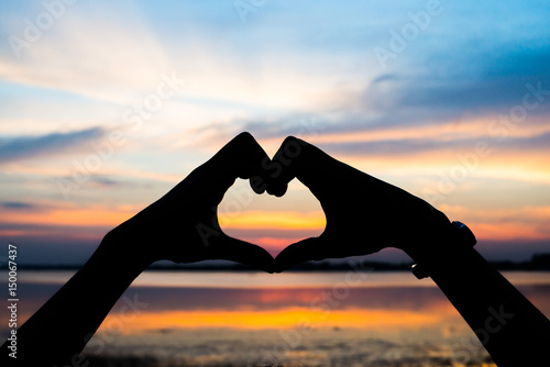 Hands forming a heart and sunset silhouette.