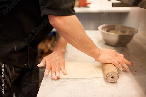 chef with rolling-pin rolling dough at kitchen