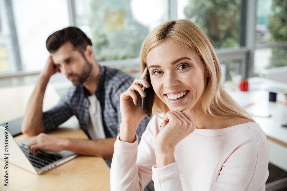 Two colleagues in office. Woman talking by phone.