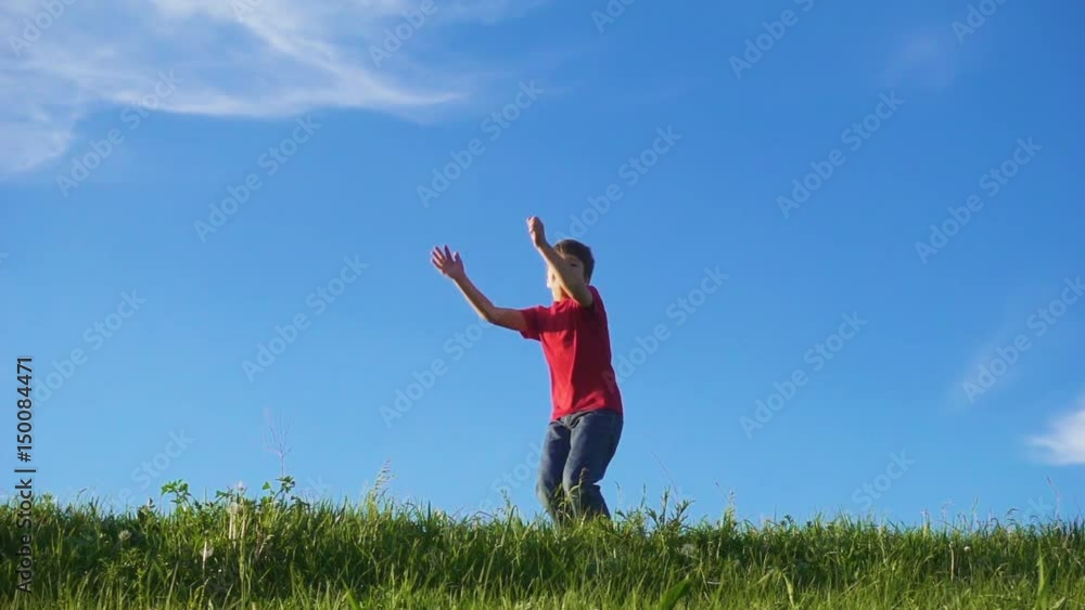Happy boy jumping on green grass hill against blue sky Happy boy jumping on green grass hill against blue sky