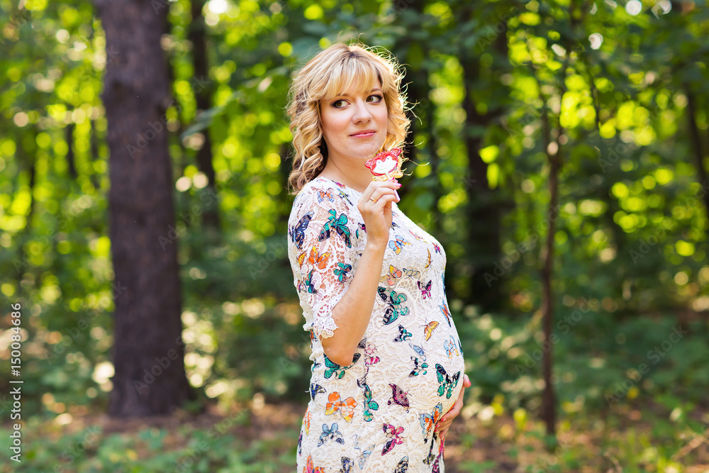 Outdoor portrait of young pregnant woman holding a lollipop in summer nature