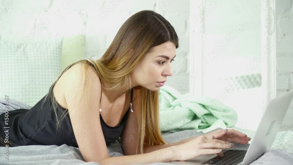 Young woman laying on a bed and using her laptop closeup Young woman laying on a bed and using her laptop closeup