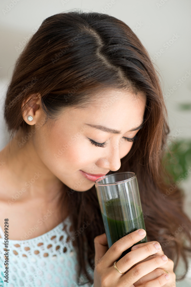 Pretty young asian woman holding green fresh vegetable juice or smoothie from glass at home Pretty young asian woman holding green fresh vegetable juice or smoothie from glass at home