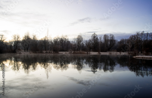 The sky reflects on the water of a lake at daybreak as winter comes to an end