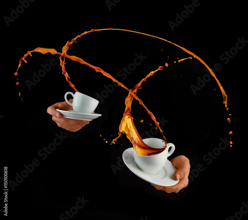 Man hands holding porcelaine cups with splashing liquid of coffee or tea, isolated on black backround