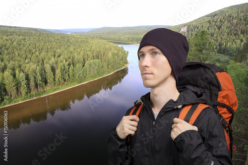 Young man with a backpack stands in front of a river.