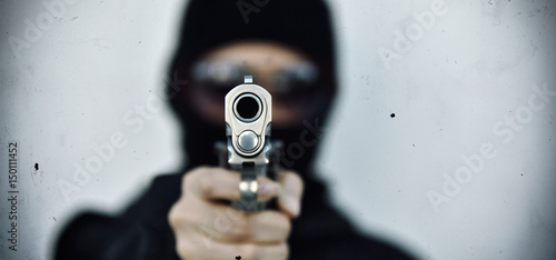 Criminal robber with aiming gun, Bad guy in hood holding pistol handgun. photo