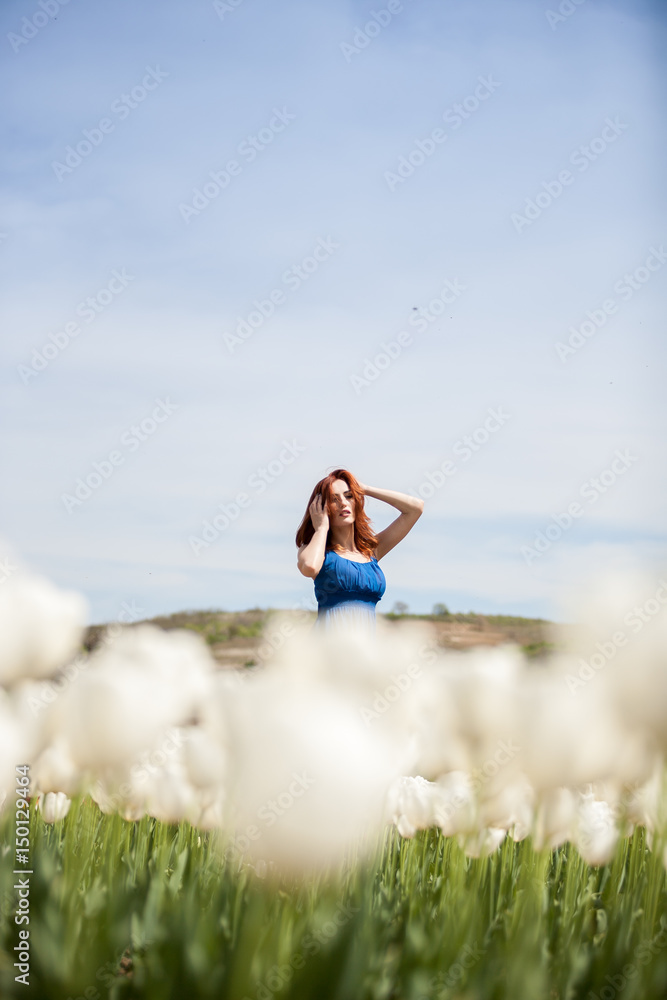 Attractive beautiful woman in blue dress in tulip field in sunny summer day. Beautiful girl in springtime