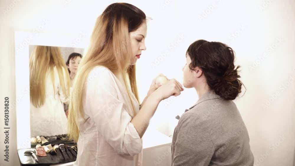 Young makeup artist applying base to the young woman's face Young makeup artist applying base to the young woman's face