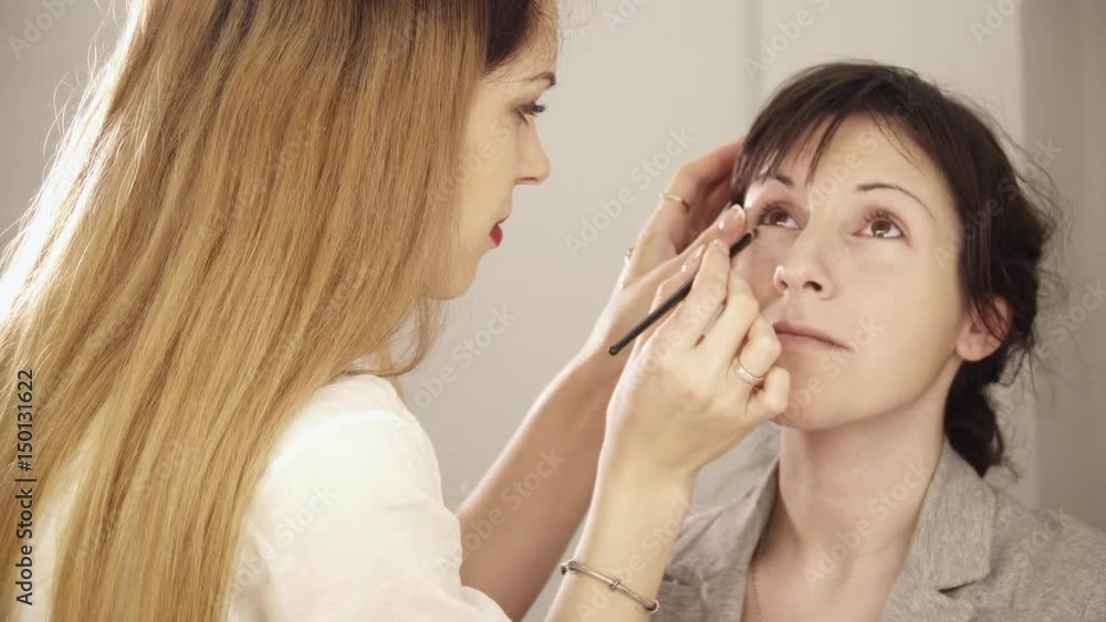 Young makeup artist applying base with brush to the face Young makeup artist applying base with brush to the face