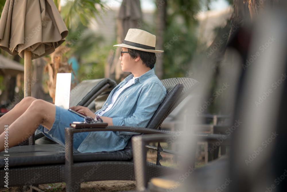 Young Asian man using laptop computer for outdoor working at resort, digital nomad lifestyle concepts Young Asian man using laptop computer for outdoor working at resort, digital nomad lifestyle concepts