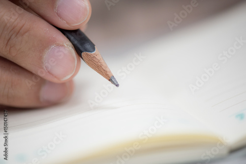 man s hand holding a pencil to writing on paper