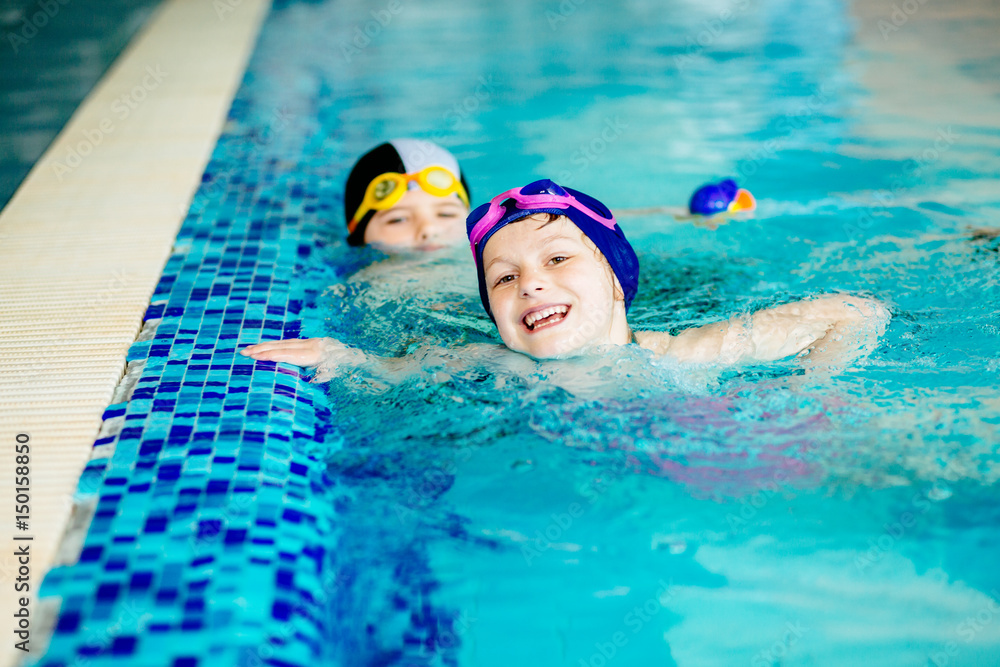 Two funny children smilling and swimming in sport pool indoors.