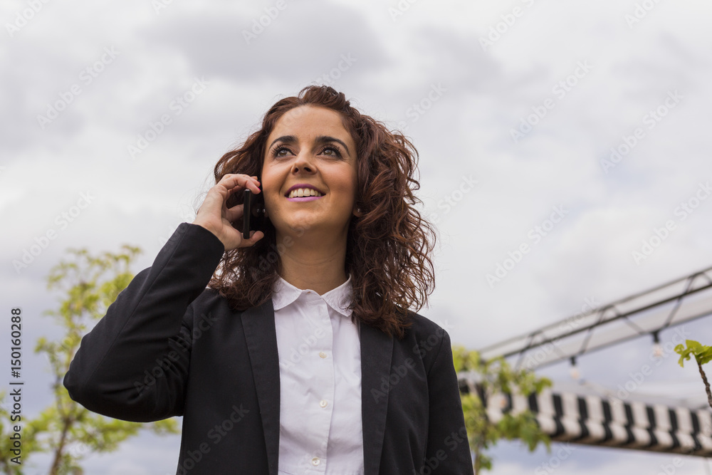 portrait of a Happy young beautiful woman smiling and talking on her mobile phone. Business woman on a terrace. Cloudy background. Working. portrait of a Happy young beautiful woman smiling and talking on her mobile phone. Business woman on a terrace. Cloudy background. Working.