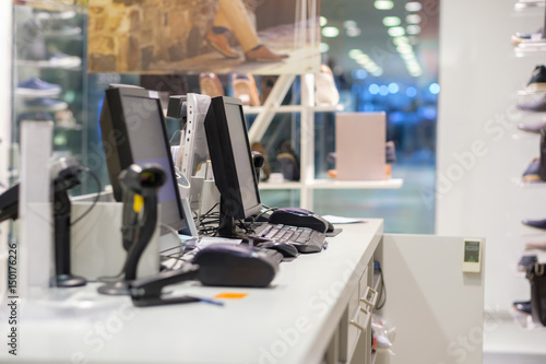 Two cash desks with computer screens and barcode scanners on white table and wall in small store