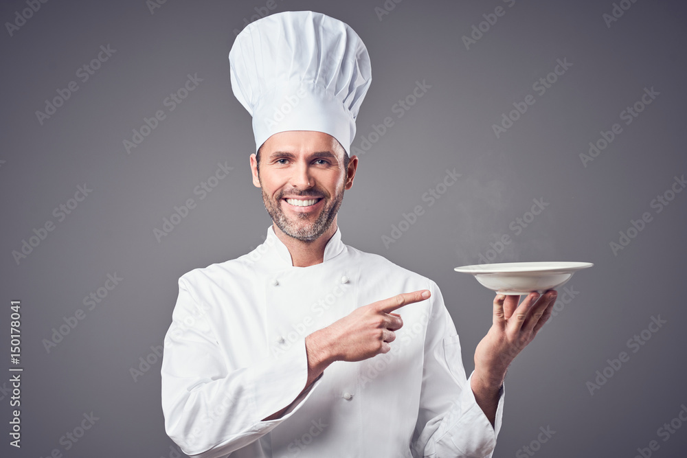 Smiling chef holding plate and pointing on it. Isolated Smiling chef holding plate and pointing on it. Isolated