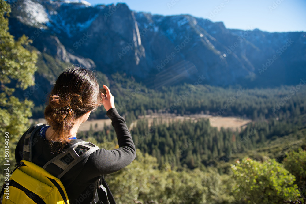 Female tourist take a photograping of Yosemite Valley with pine forest in foreground sun light lay on the forest