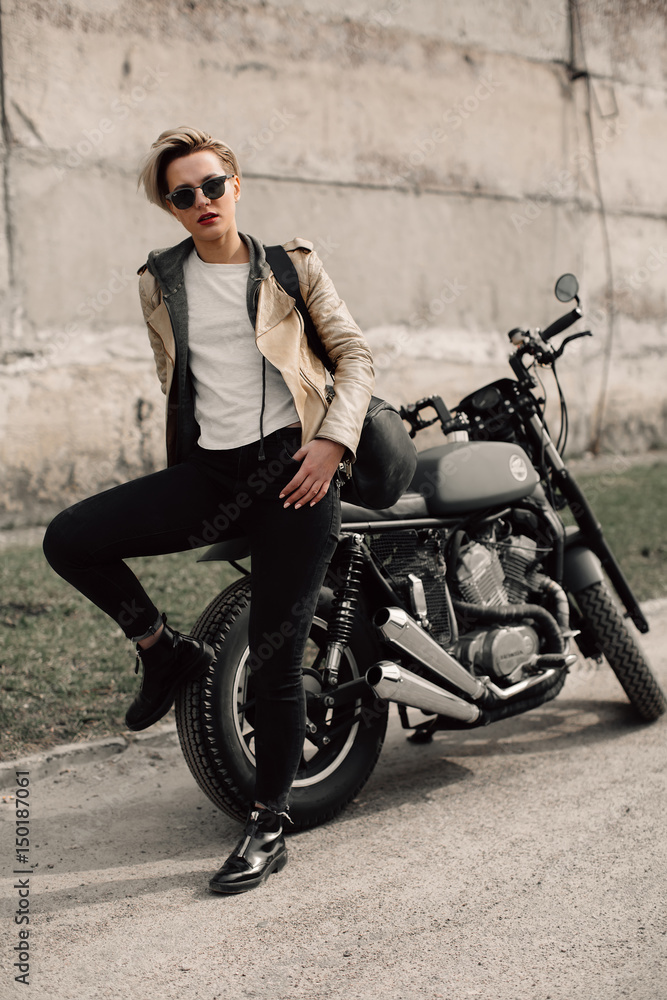 Woman sitting on his motorcycle. Motorcycle near a grey wall. girl