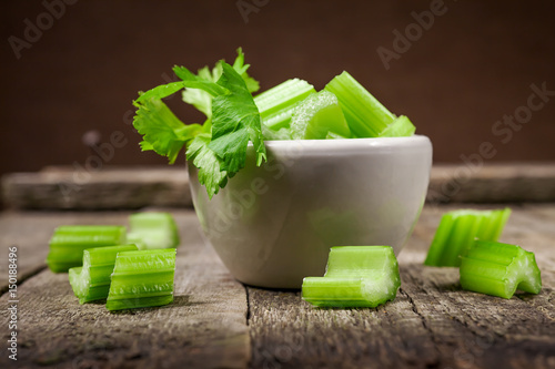 Fresh sliced celery in a white bowl on a vintage wooden background, selective focus