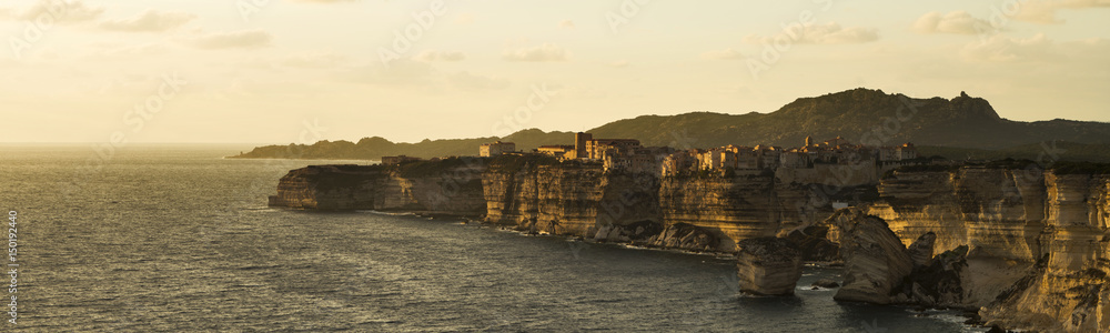 Panoramic image of the village of Bonifacio in Corsica on its rocky limestone coastline during a yellow sunset.