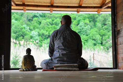 Buddhist Meditation. Older man meditating in a wooden house. Senior man practicing meditation with a Buddha Statue.