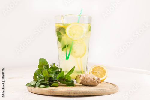 A glass decanter with a summer refreshing lemonade made of lemons and ginger with mint added on a white wooden background. Detox water. Ingredients. Cleaning the body of toxins, vitamins