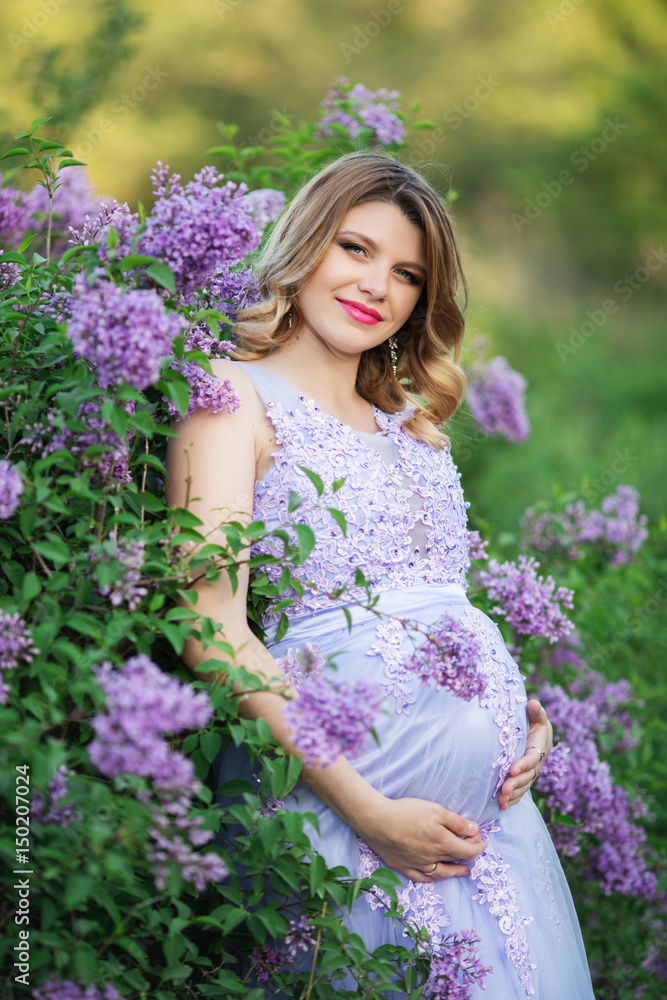 Fototapeta premium Pretty pregnant woman in blossom lilac garden