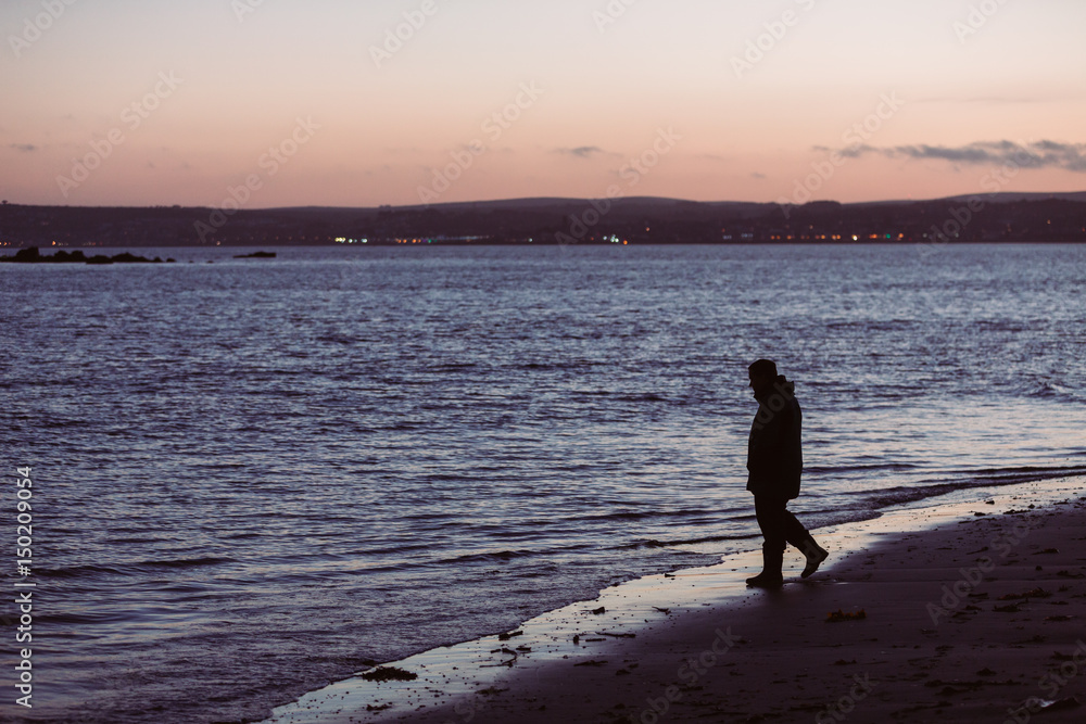 Naklejka premium Man walking on beach at night looking into the sea with desire