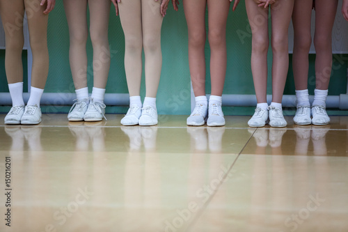 Children legs of aerobic athletes wearing in white sport boots standing in line in gym