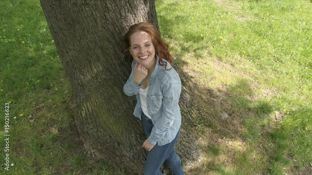 glückliche frau steht unter einem großen baum und schaut lachend nach oben