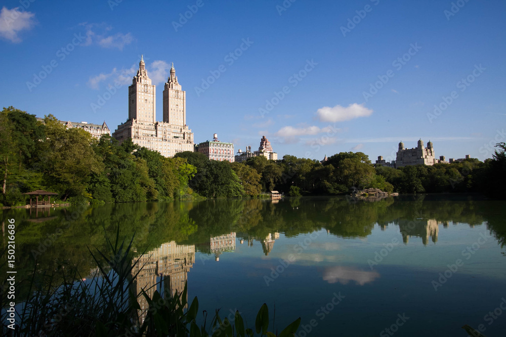 Buildings of Manhattan reflect on calmly water at Central Park with blue sky in summer
