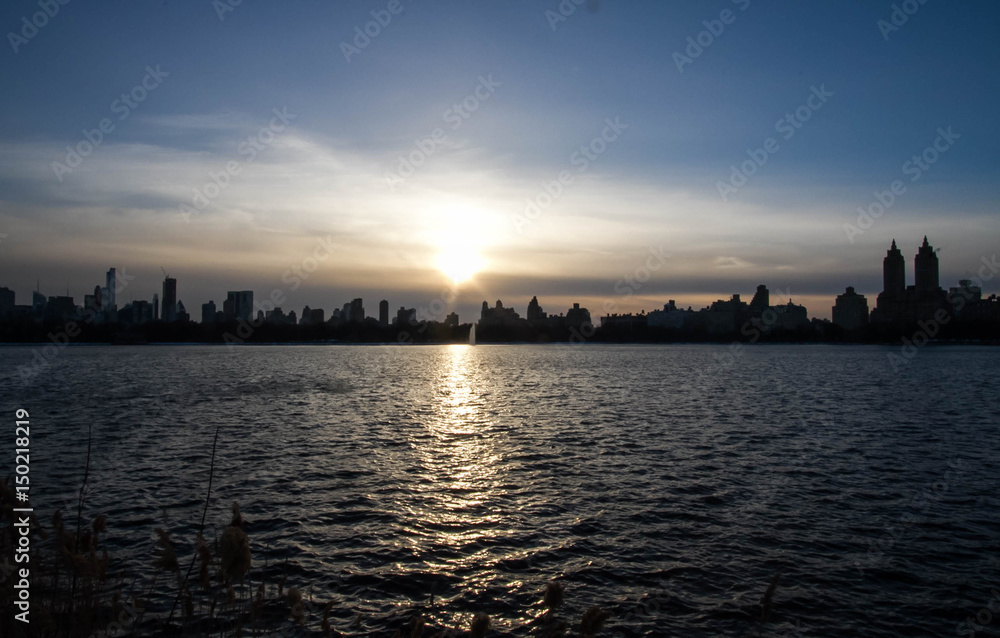 Silhouette buildings in Manhattan with blue sunset sky and reflective lake