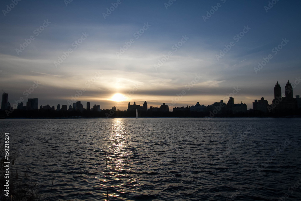 Sunset over silhouette buildings and lake with blue sky