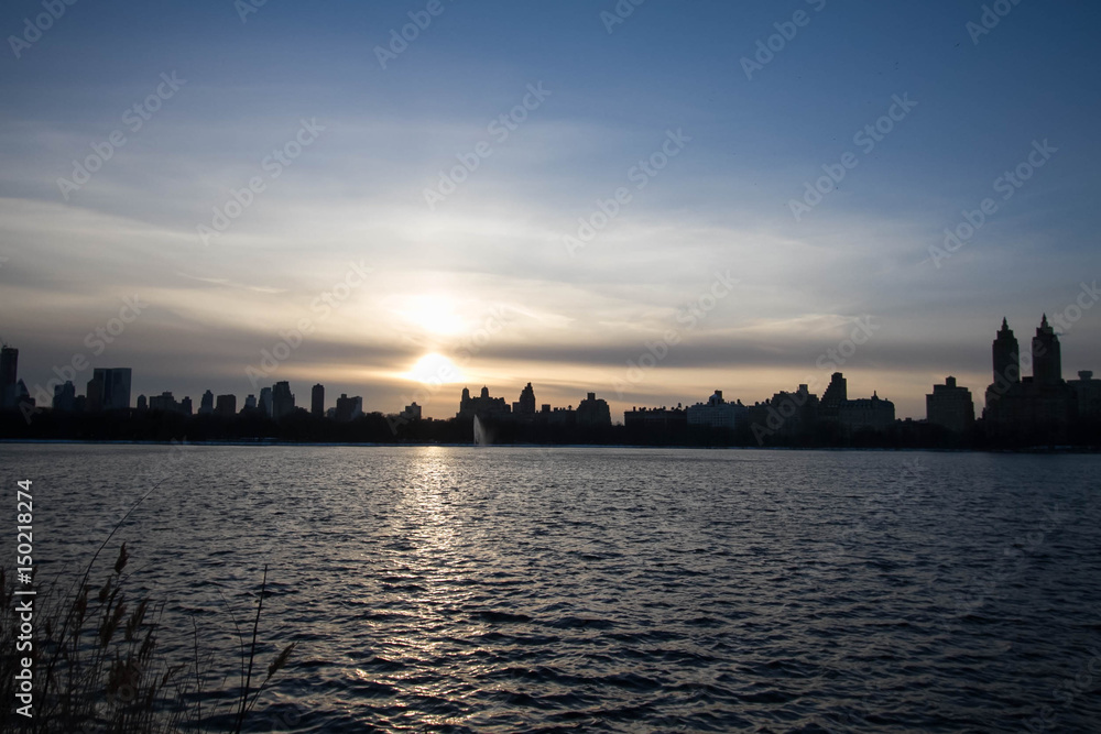 Sunset over silhouette buildings and lake with blue sky, Manhattan