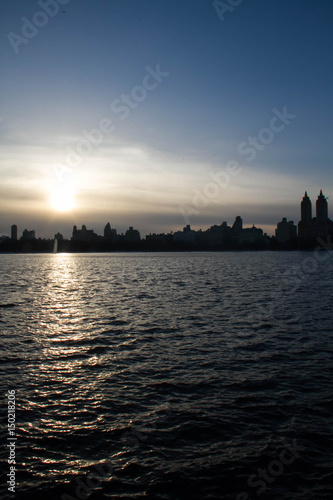 Silhouette buildings in Manhattan with blue sunset sky and dark lake