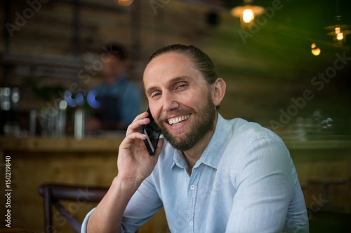 Smiling man talking on mobile phone at café