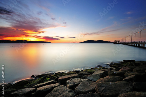 Long exposure of sunset and sea with rocky foreground.