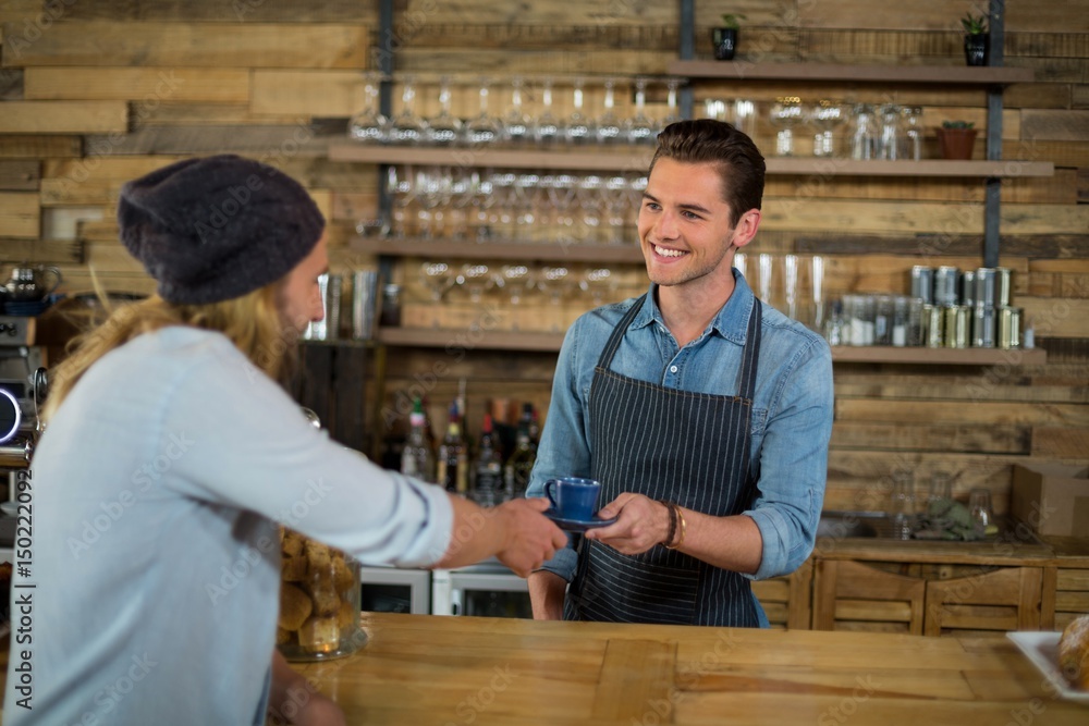 Smiling waiter serving cup of coffee to man at counter Smiling waiter serving cup of coffee to man at counter