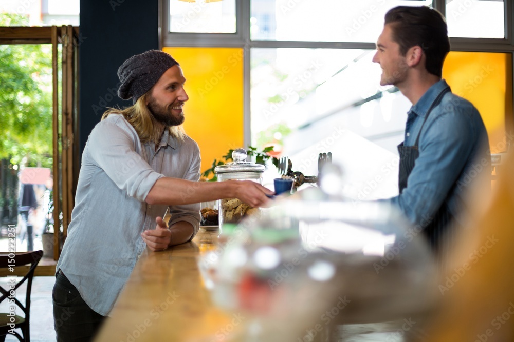 Φωτογραφία Smiling waiter serving cup of coffee to man at counter