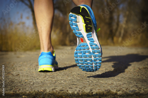 Back view of male muscular feet in sneakers walking on sidewalk in spring sunny day