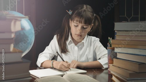 Eight years school girl writing in her notebook, studying place with books and globe, education concept, 30FPS