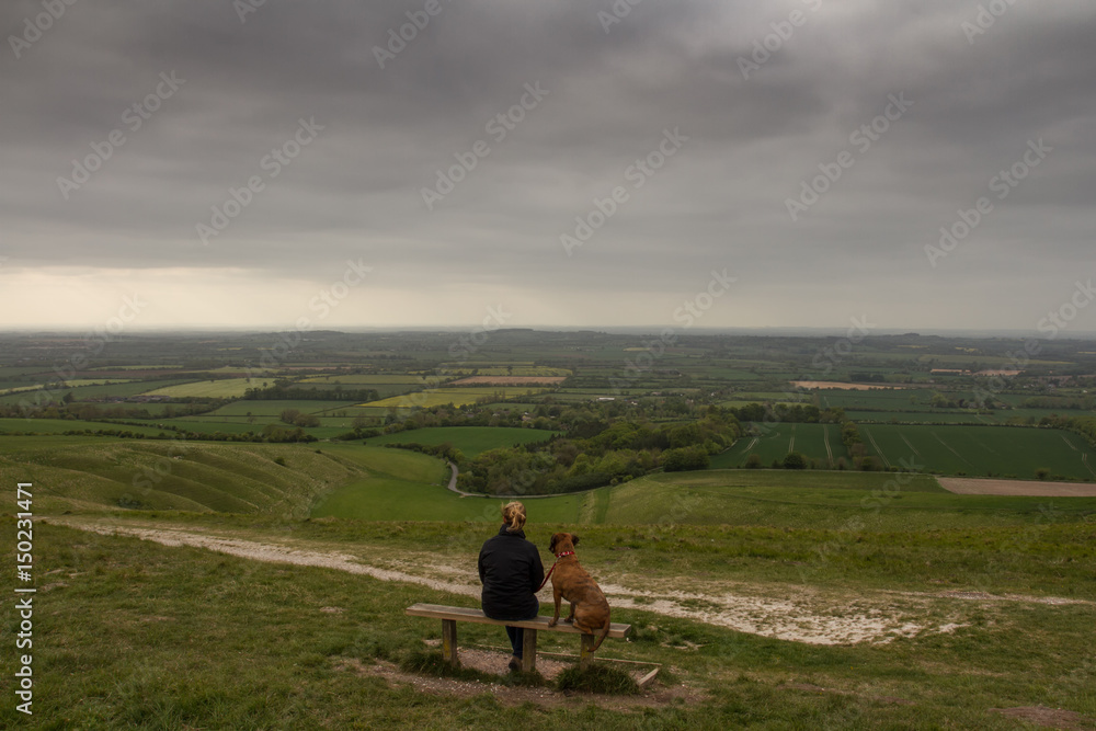 Single female takes in the view with her dog from white horse hill, Uffington, Oxfordshire, UK
