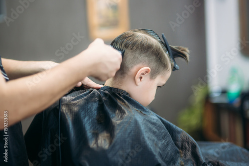 Little boy on a haircut in the barber sits on a chair.