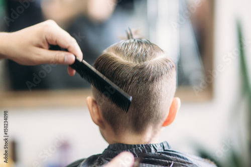 Little boy on a haircut in the barber sits on a chair. © Aleksandr